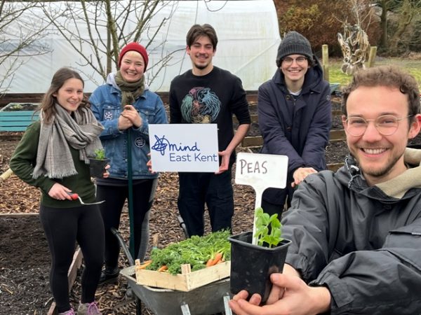A photo taken at the Kent Community Oasis Garden. There are five students there with their produce and holding the East Kent Mind logo.