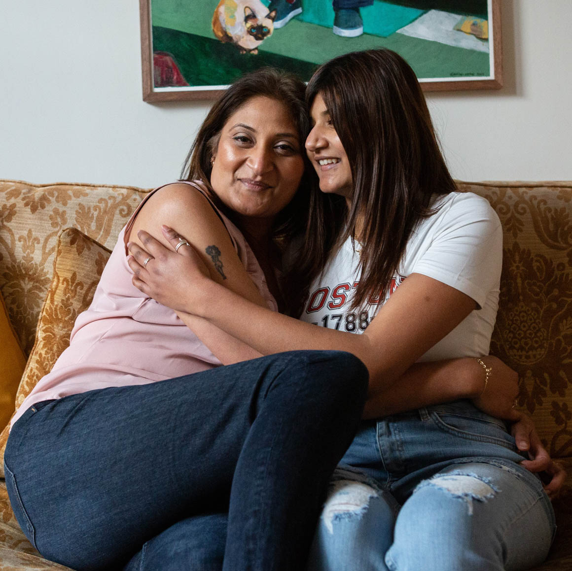 A woman and her daughter hug on a living room sofa