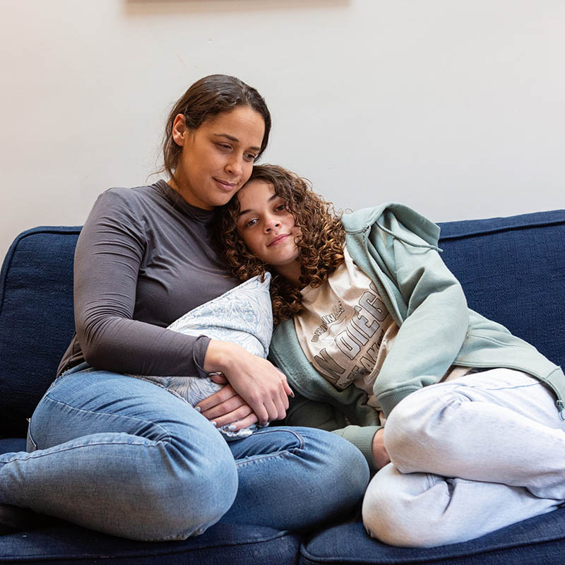 A photograph of a young mother with her daughter embracing on a living room sofa
