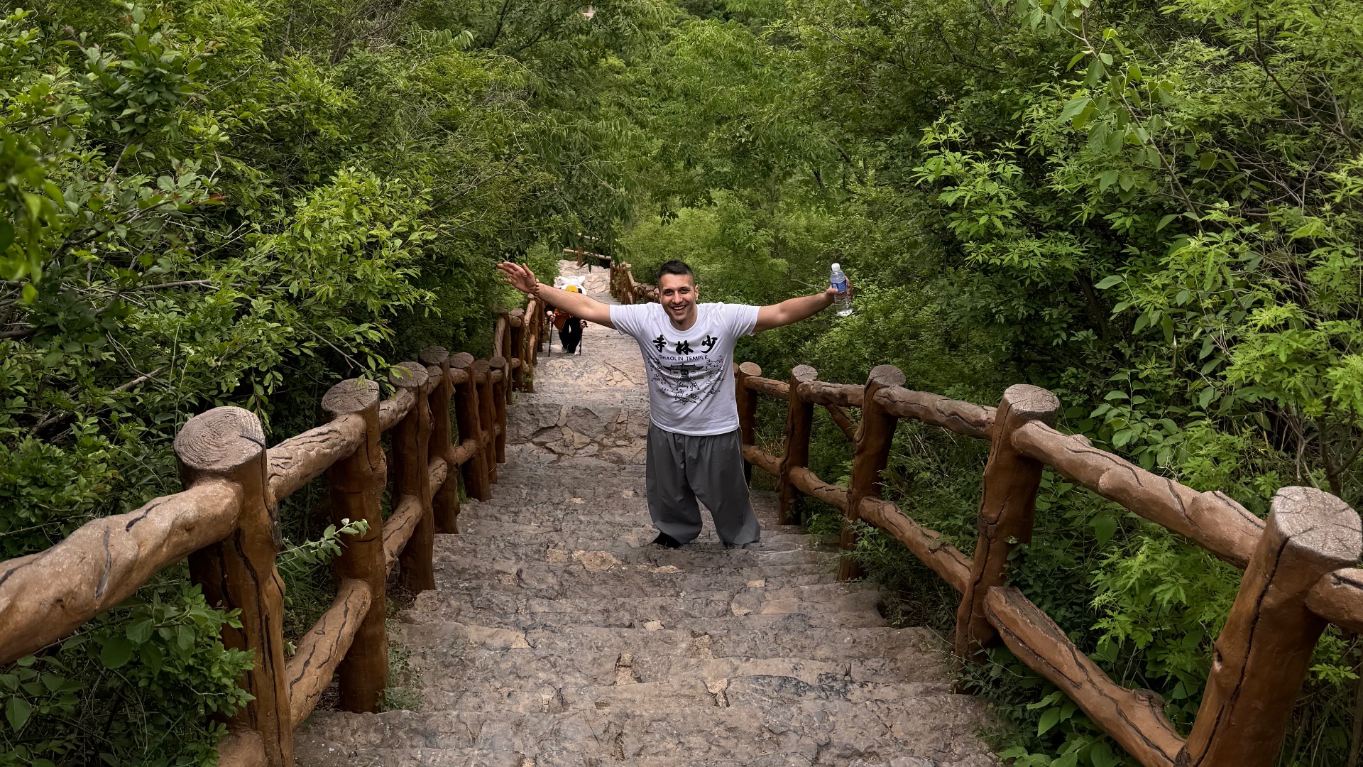 Jasdeep Sohl smiling and raising his hands as he climbs a large amount of steps in a wooded area