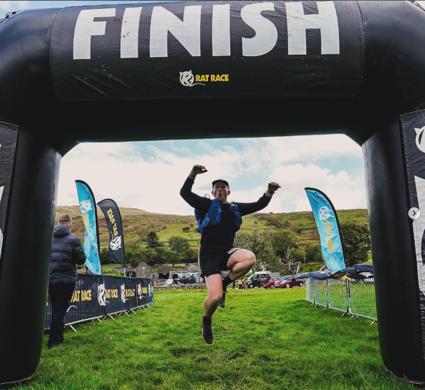 Rob Brady jumping for joy as he ends the Rat Race run under an inflatable arch that says 'FINISH'
