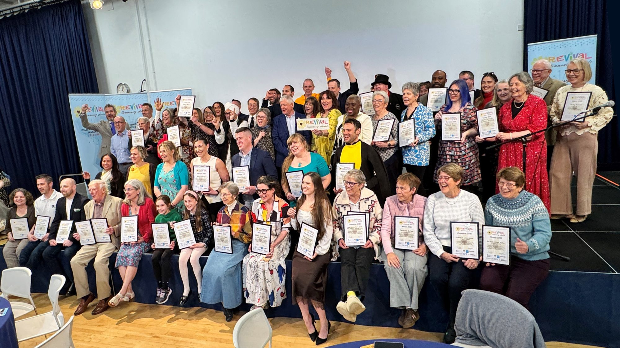 The groups of winners facing the official photographer smiling and cheering and holding either their winners or champions certificates