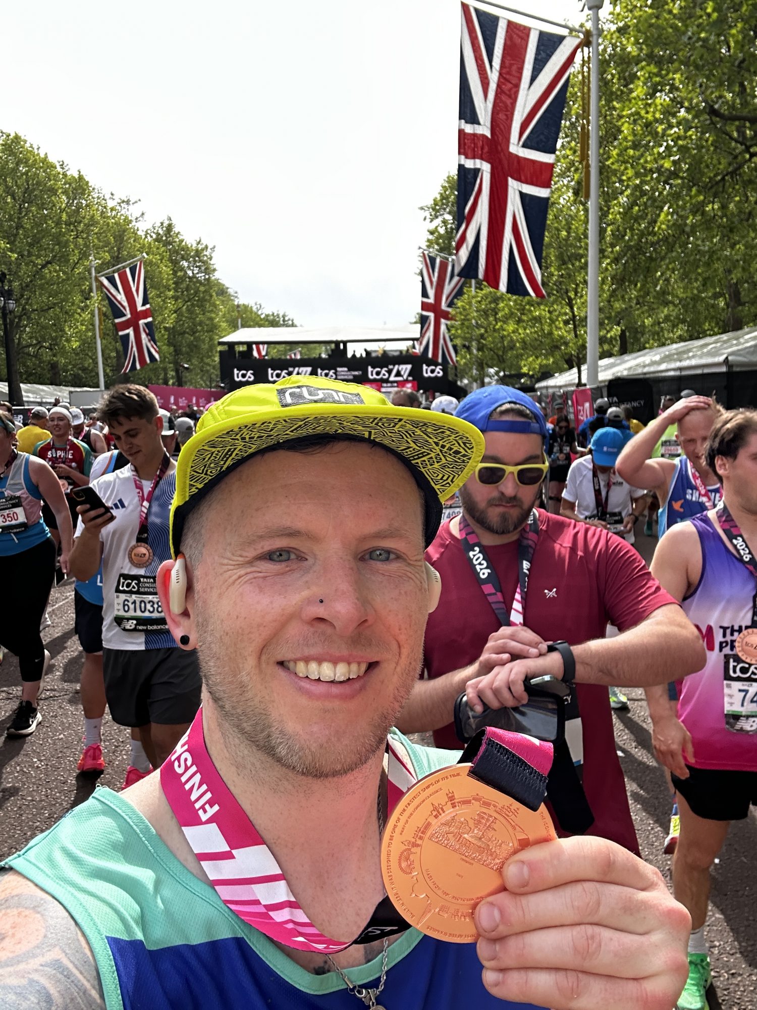 Rob Brady is smiling and holding his London Marathon medal with a group of runners behind him